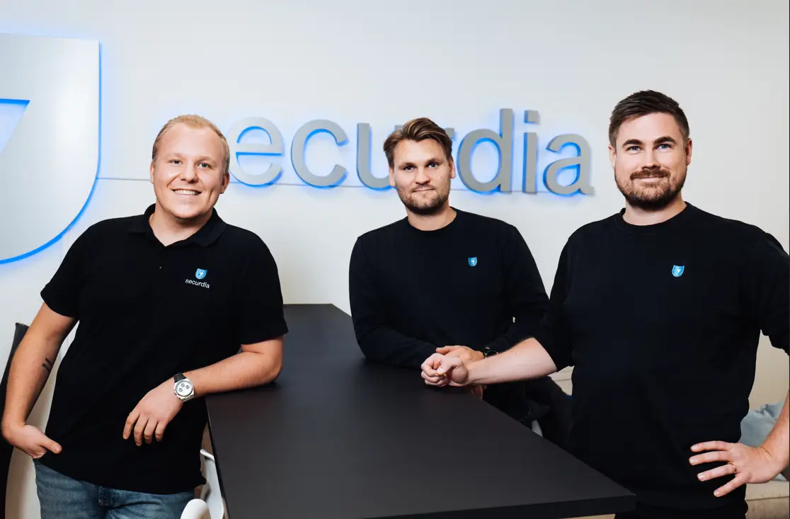 Tre män i svarta kläder står framför en vägg med företagslogga och texten "securdia".